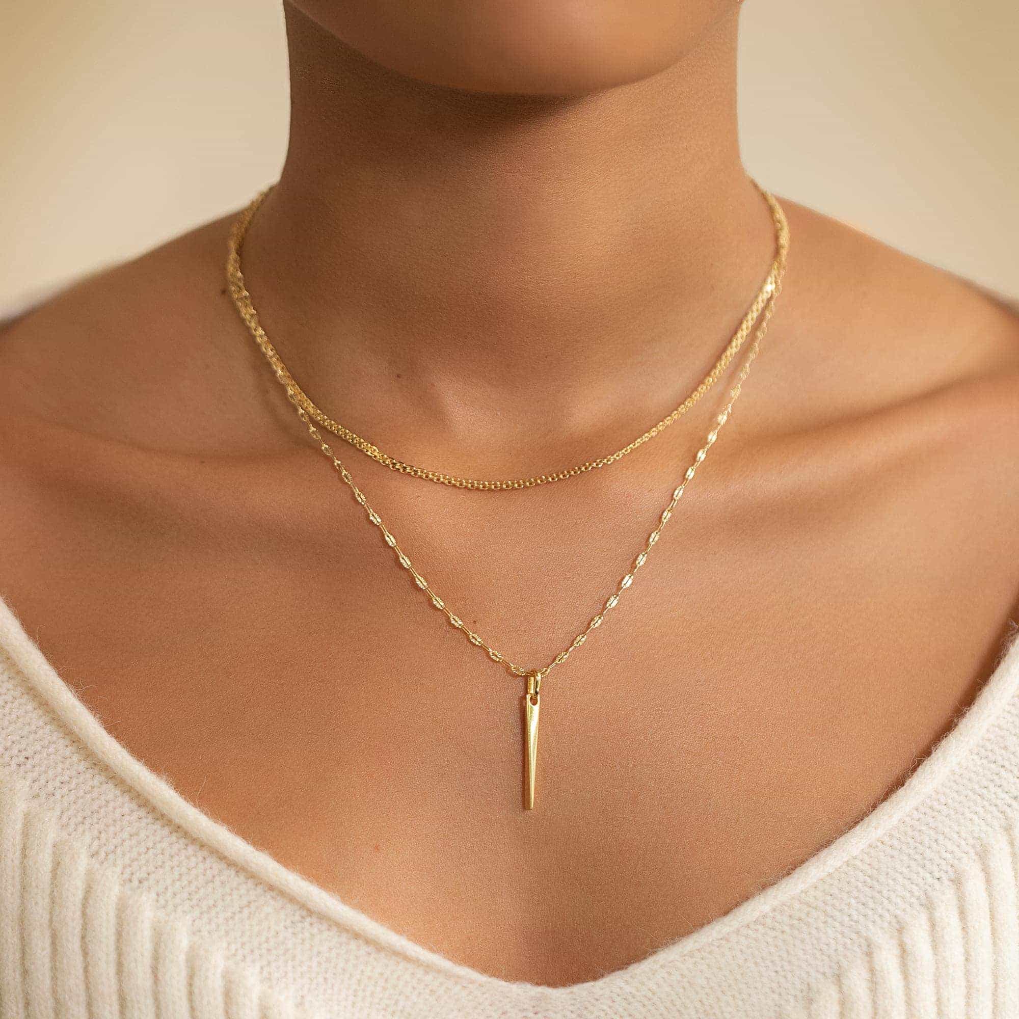 Gold vermeil tapered spike bar pendant on a layered chain, shown on a model's neckline