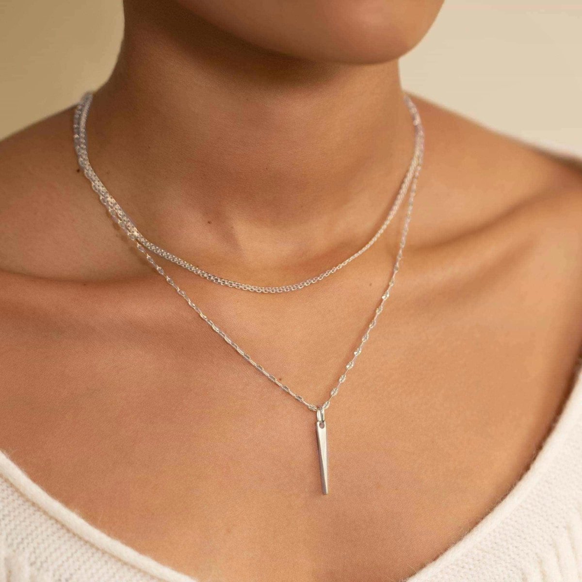 Sterling silver tapered spike bar pendant on a layered chain, shown on a model's neckline