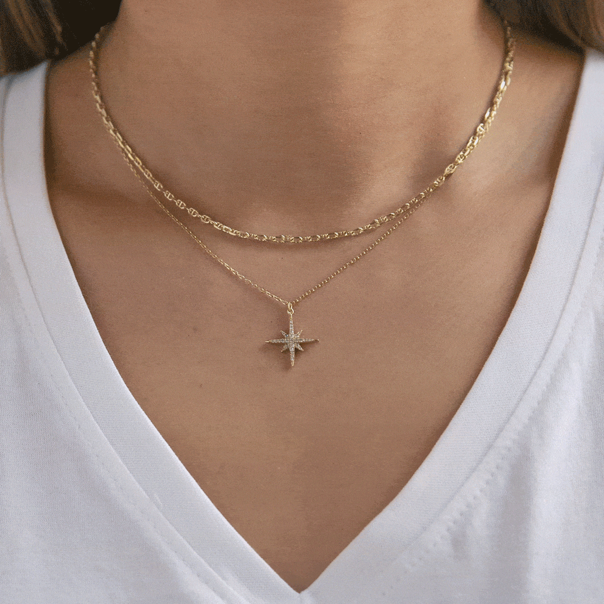 Layered gold necklaces on a model, a textured chain choker over a clear-stone starburst pendant