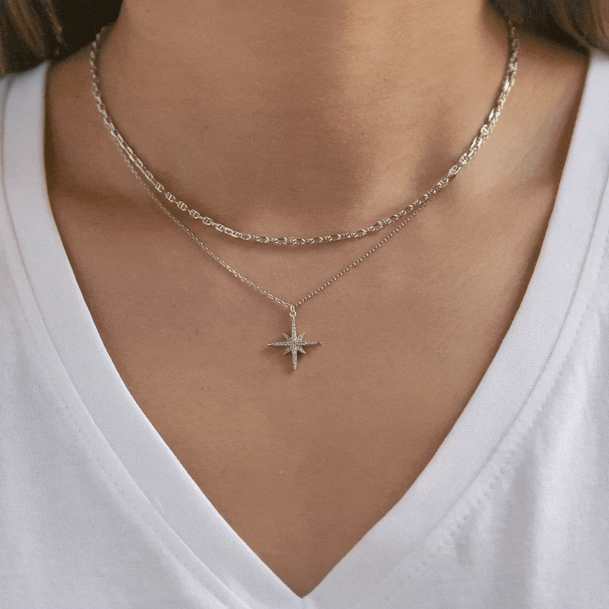 Layered silver necklaces on a model, a textured chain choker over a clear-stone starburst pendant