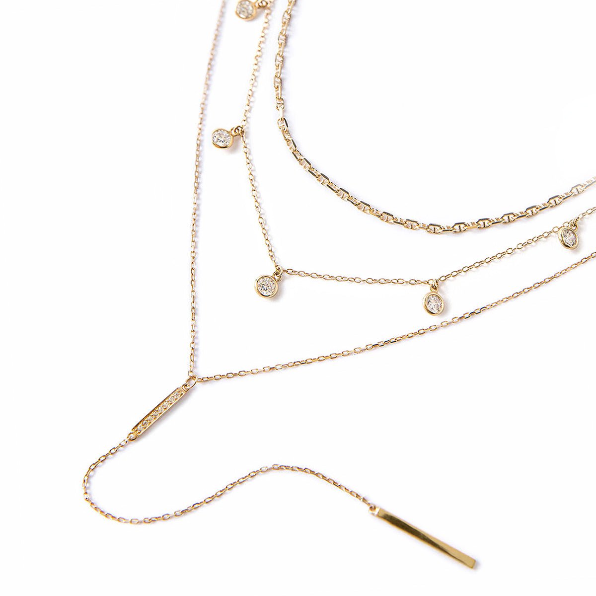 Gold vermeil layered necklace trio with bezel-set clear crystal drops and a bar lariat, on a white background