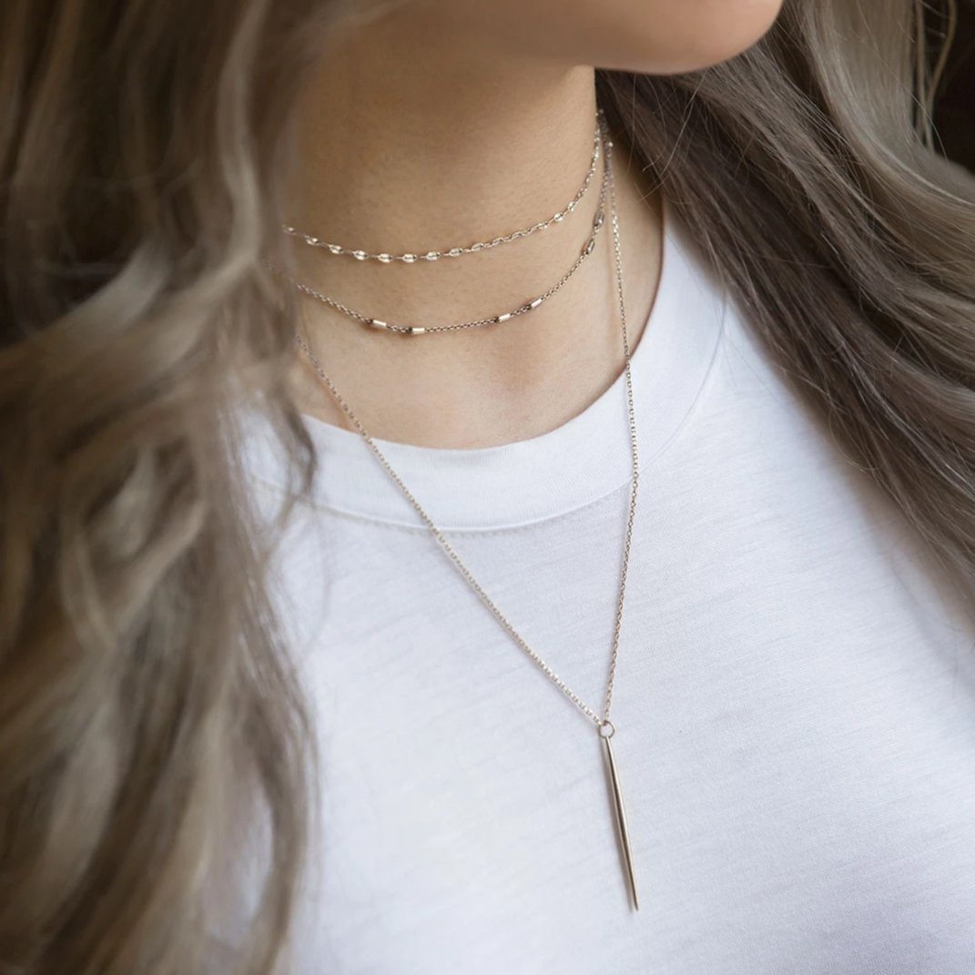 Sterling silver layered necklace with a long slim needle bar pendant, shown on a model's neckline