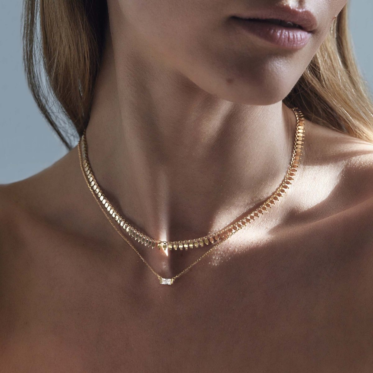 Gold vermeil layered duo with a clear baguette stone pendant, shown on a model's neckline