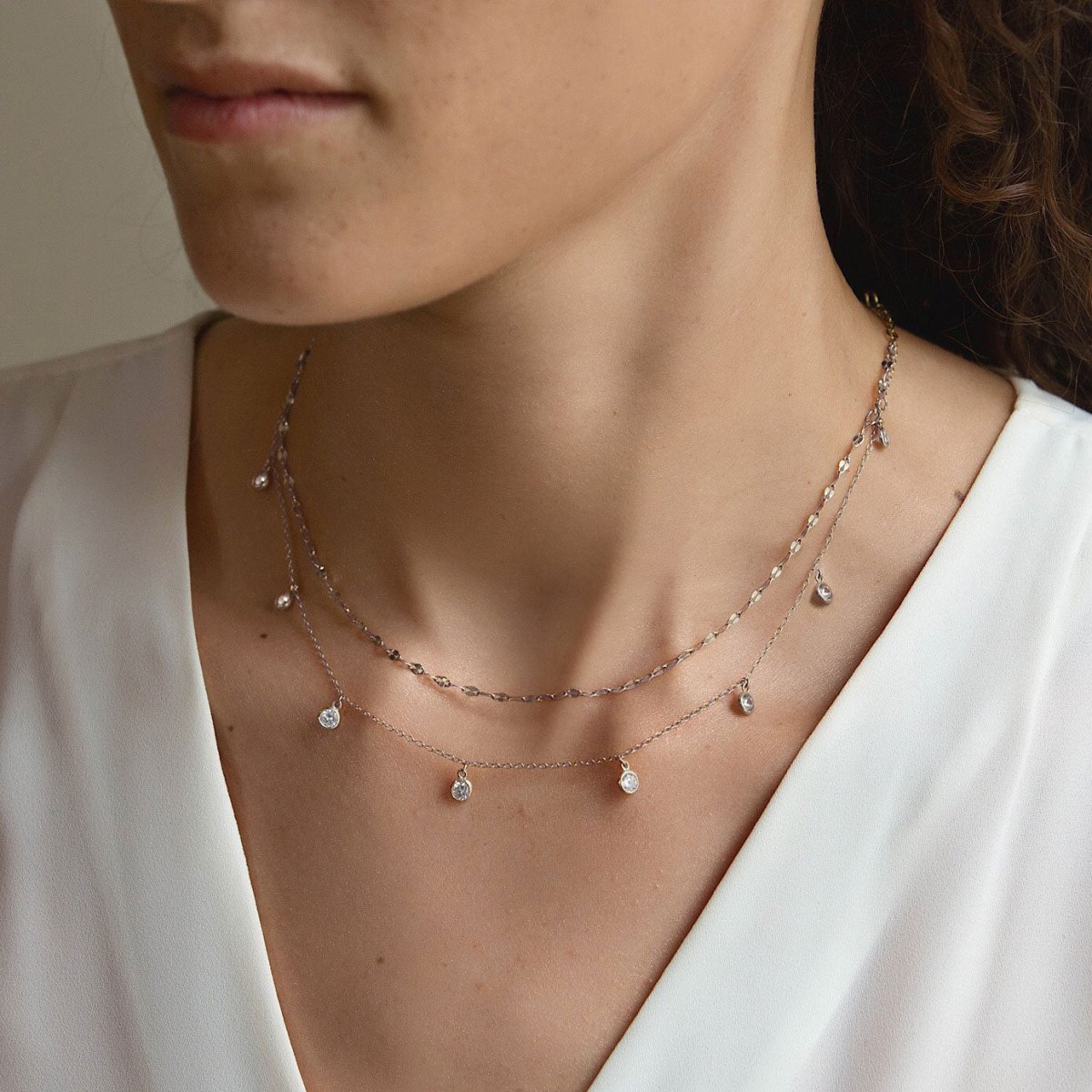 Sterling silver layered necklace duo with clear stone charms, shown on a model's neckline