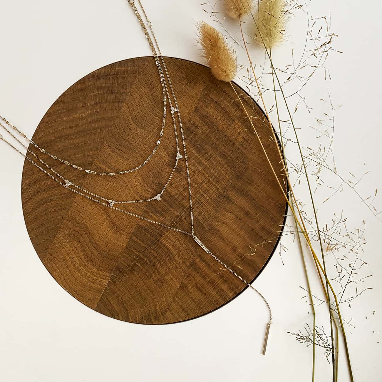 Sterling silver clover bar lariat layered duo with clear stones, laid on a wood disc