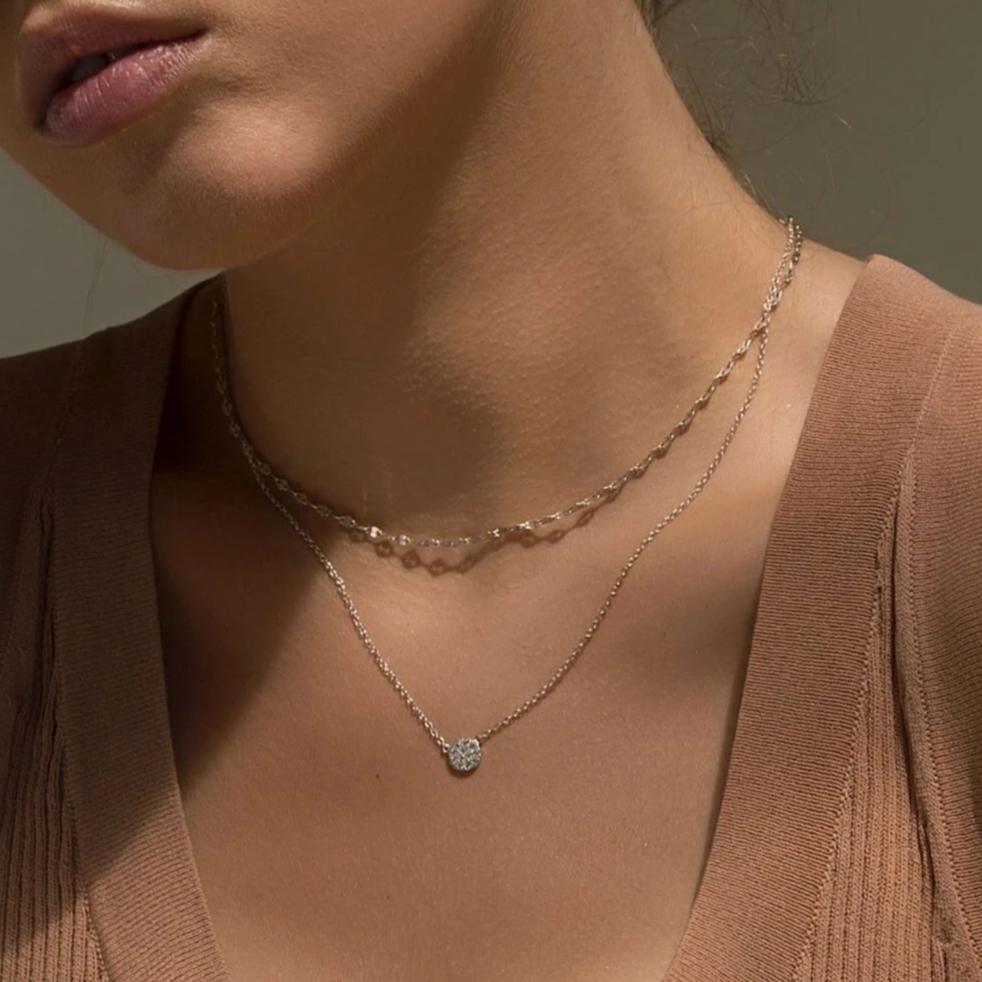 Sterling silver layered necklace duo with a round pavé disc pendant set with clear stones, on a model's neckline