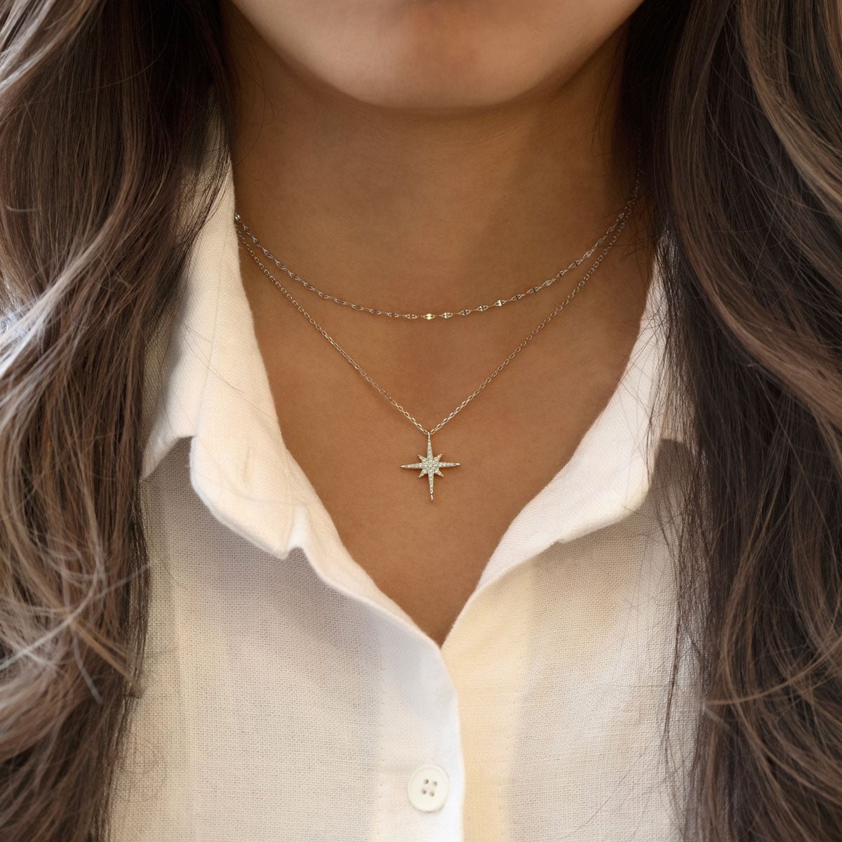 Sterling silver starburst pendant with clear stones, layered over a white shirt on a model's neckline
