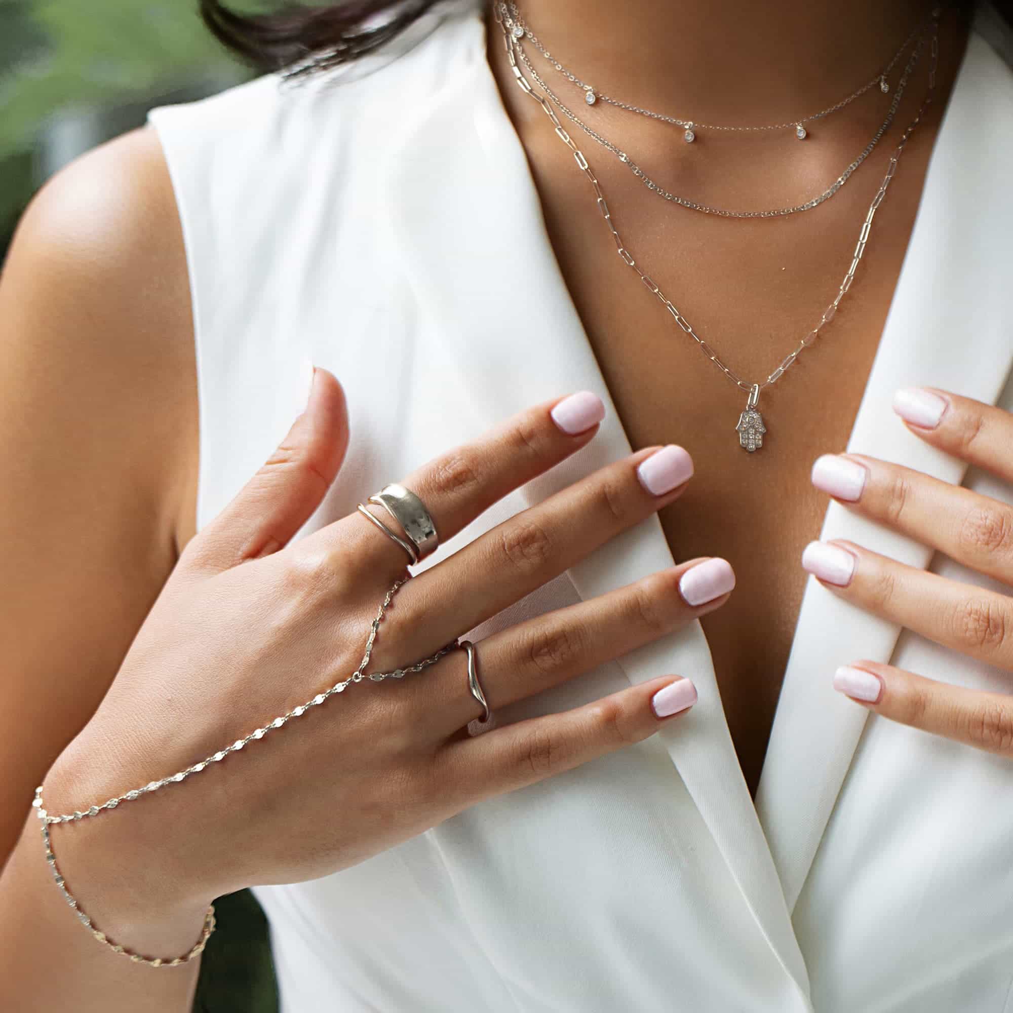 Layered silver necklaces, rings and a hand chain shown on a model's neckline and hand