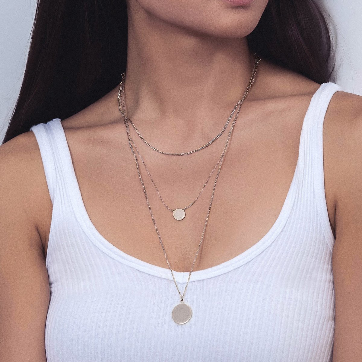Sterling silver Figaro disc trio necklace layered with disc pendants, shown on a model's neckline