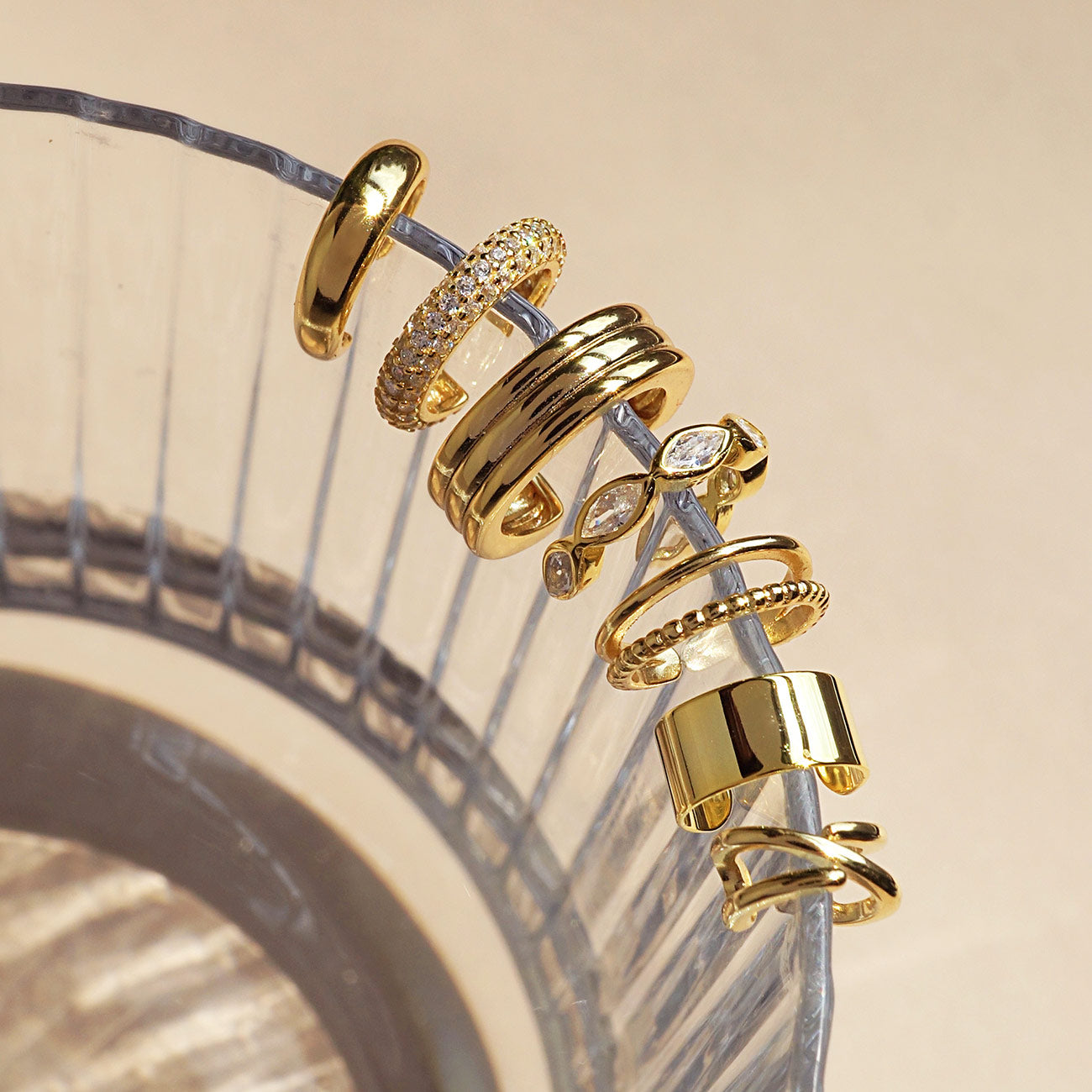 Assorted gold ear cuffs lined up along the edge of a ribbed glass dish