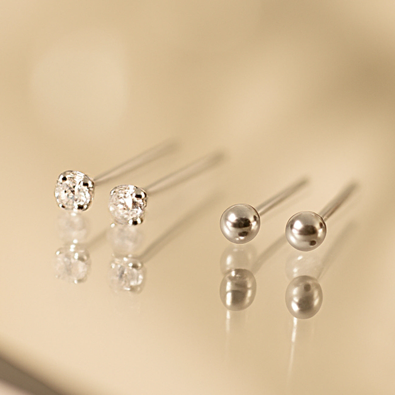 Two pairs of tiny silver stud earrings, one crystal and one polished ball