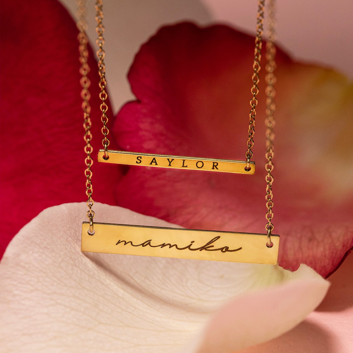 Gold vermeil name bar necklaces engraved with names, layered close-up on rose petals