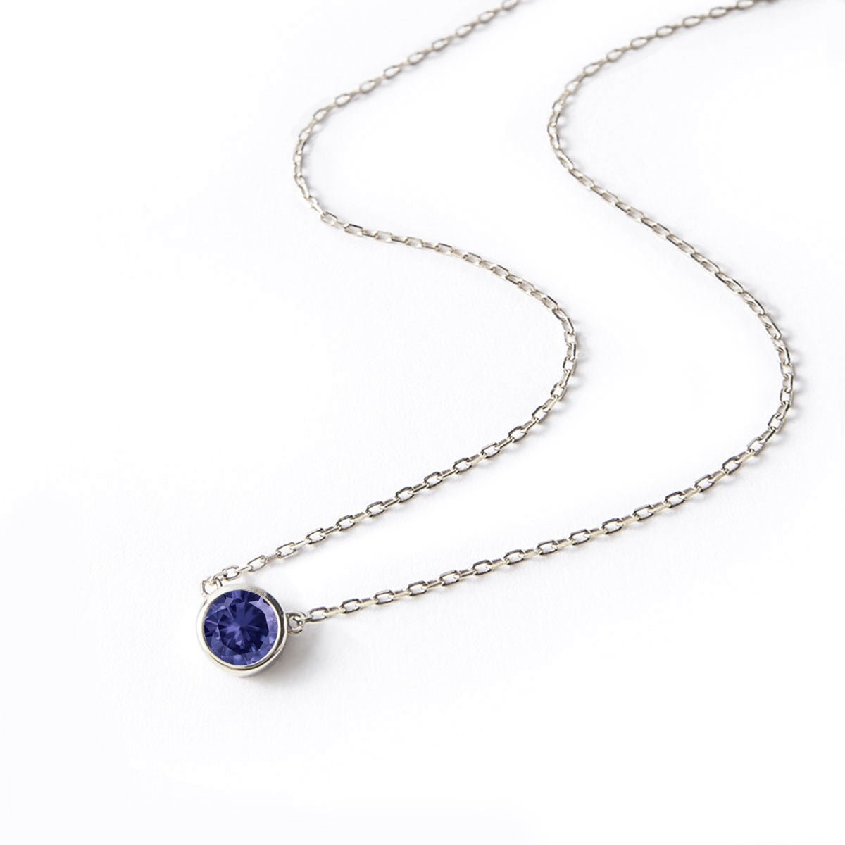 Sterling silver solitaire necklace with a round bezel-set blue sapphire, on a white background