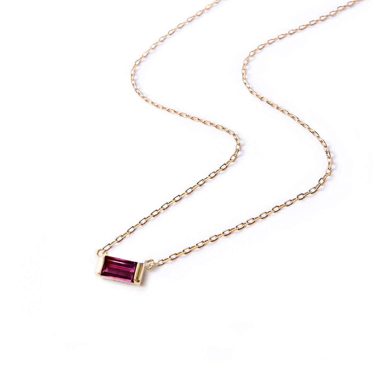 Gold vermeil necklace with a red ruby baguette pendant on a thin chain, laid on a white background