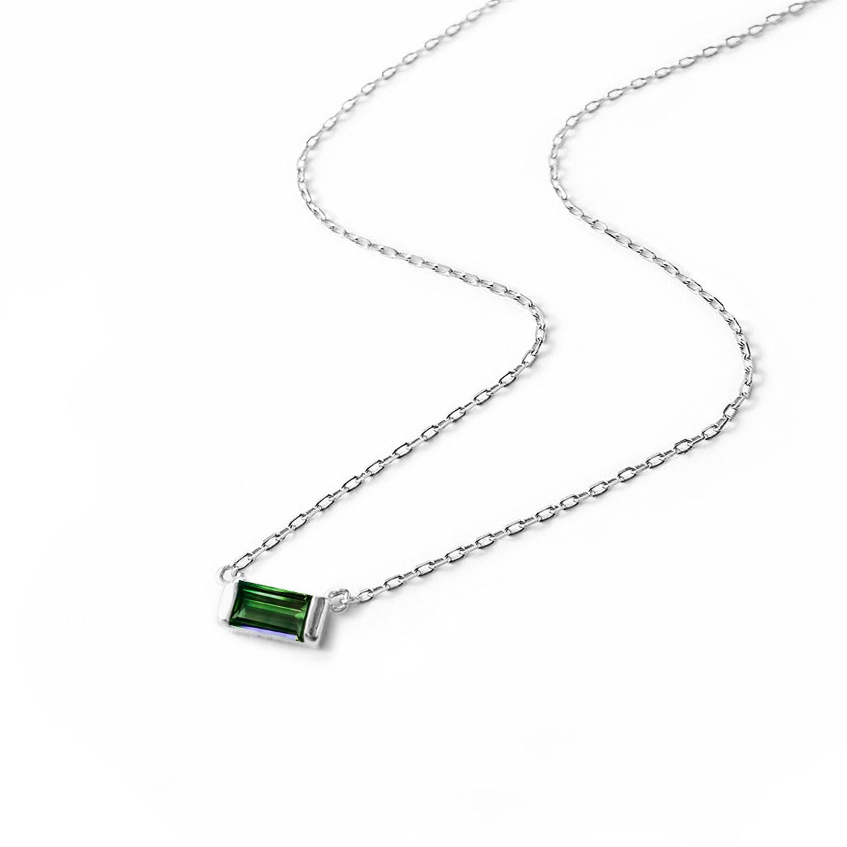 Sterling silver necklace with a green emerald baguette pendant on a thin chain, laid on a white background