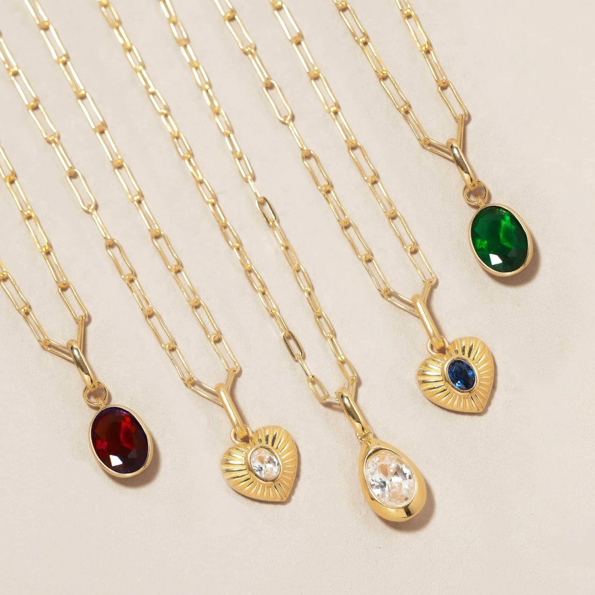 Gold vermeil oval green emerald charm with red, clear and blue charms on chains, on a cream background