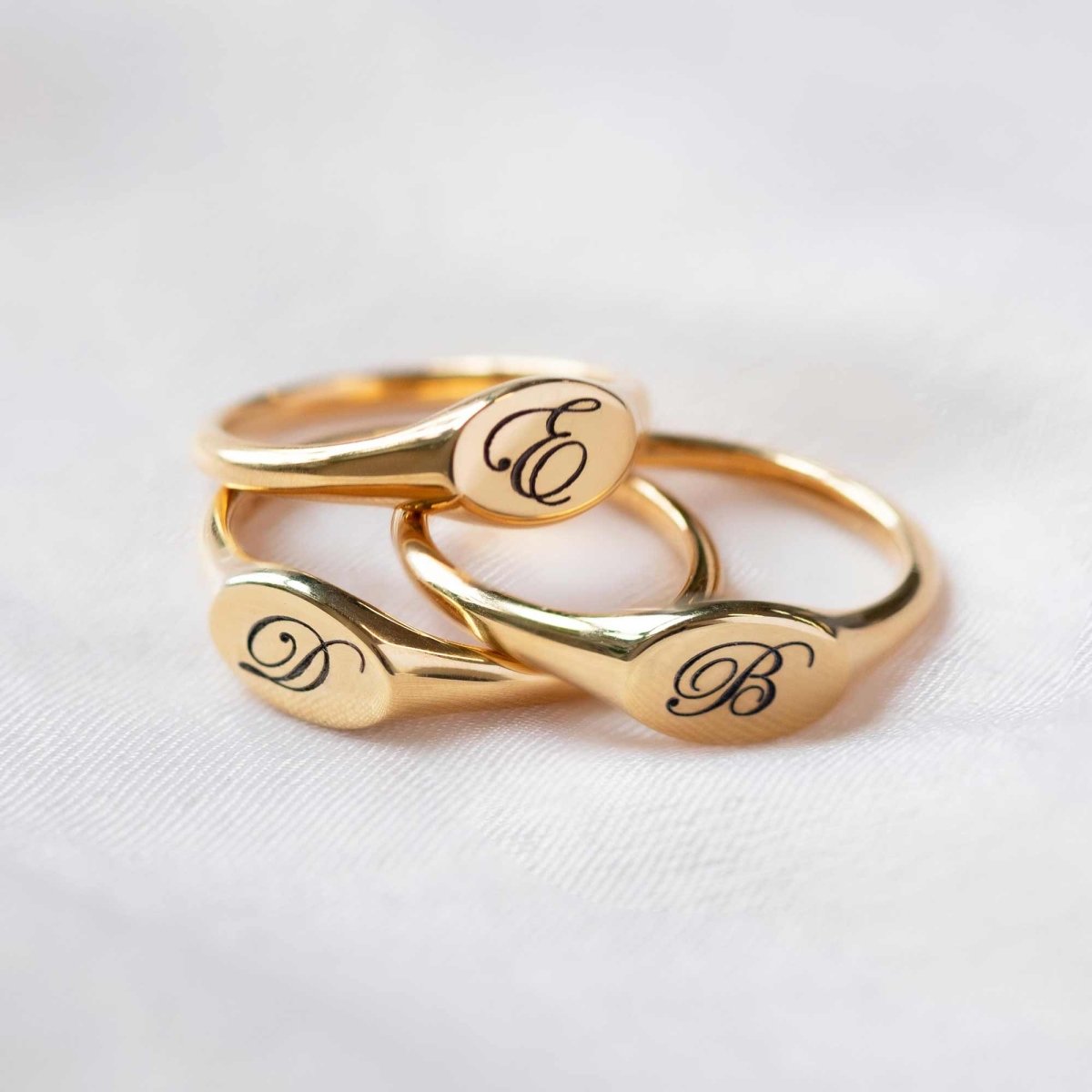 Gold vermeil oval signet rings engraved with initials, stacked on a soft white fabric