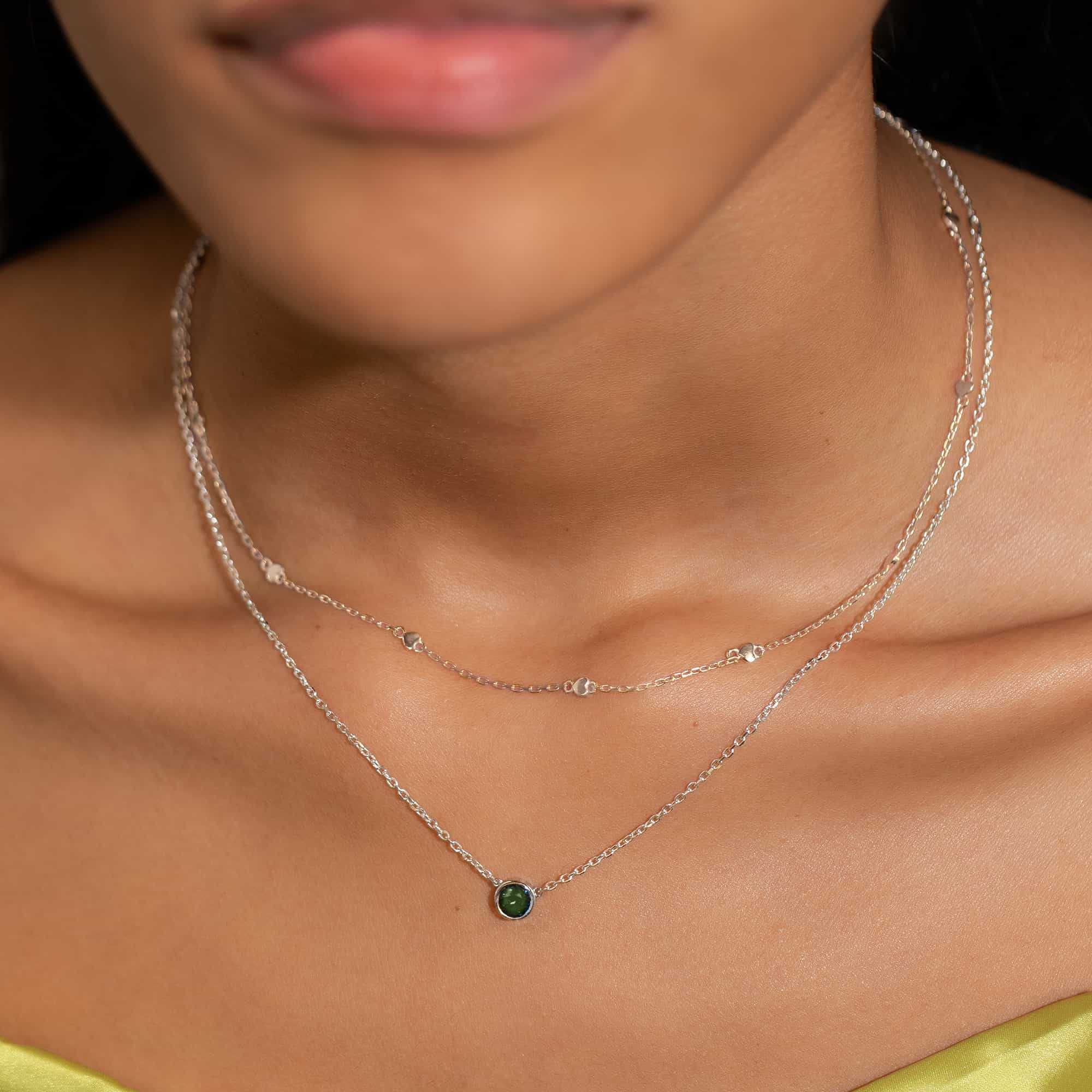 Silver heart-station chain layered with a green-stone solitaire necklace on a model's neckline