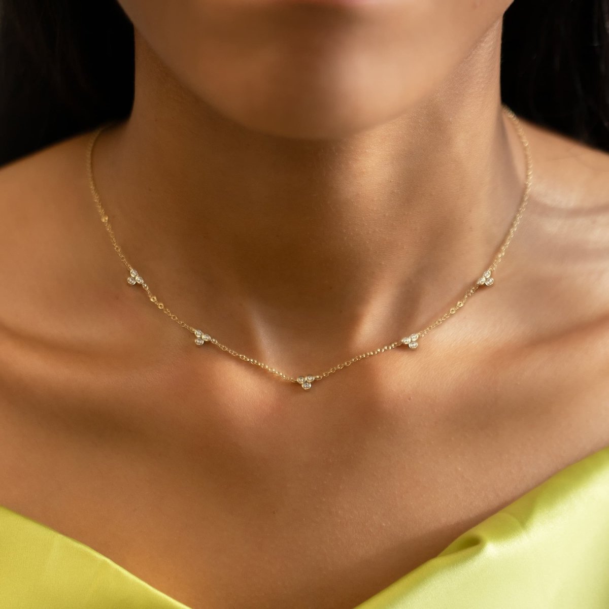 Gold vermeil necklace with three-stone clover clusters of clear stones, shown on a model's neckline