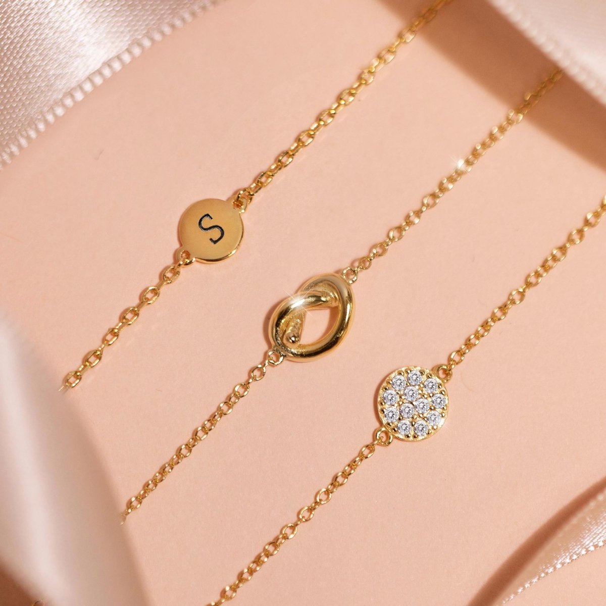 Gold vermeil love knot chain bracelet layered with an initial disc and pavé disc