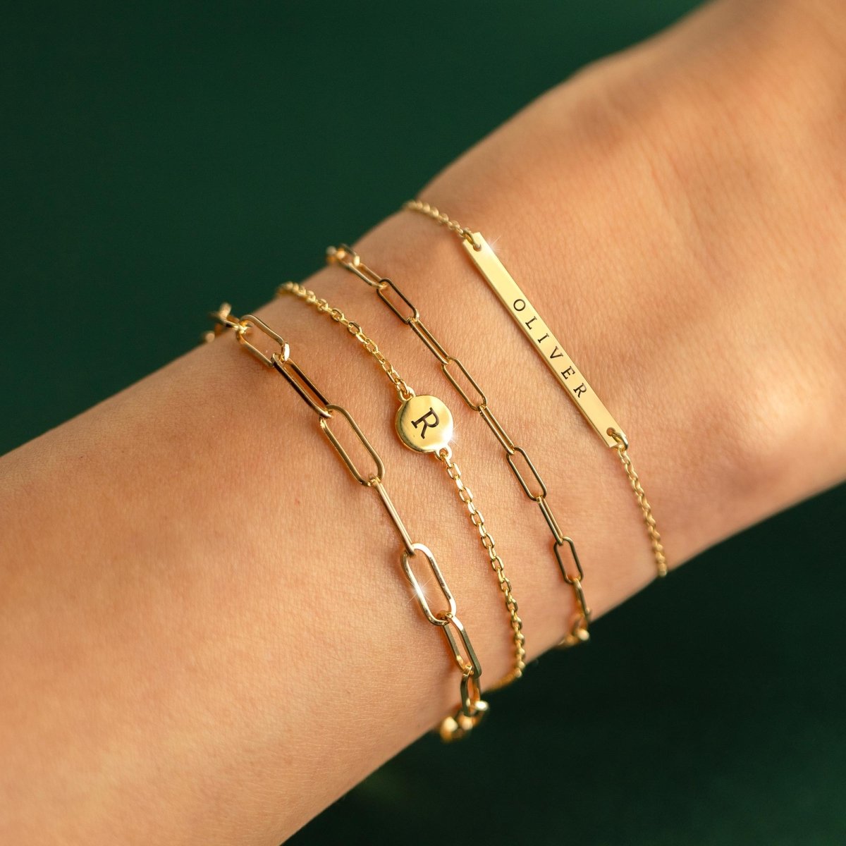 14K gold disc bracelet engraved with an initial, shown stacked on a model's wrist