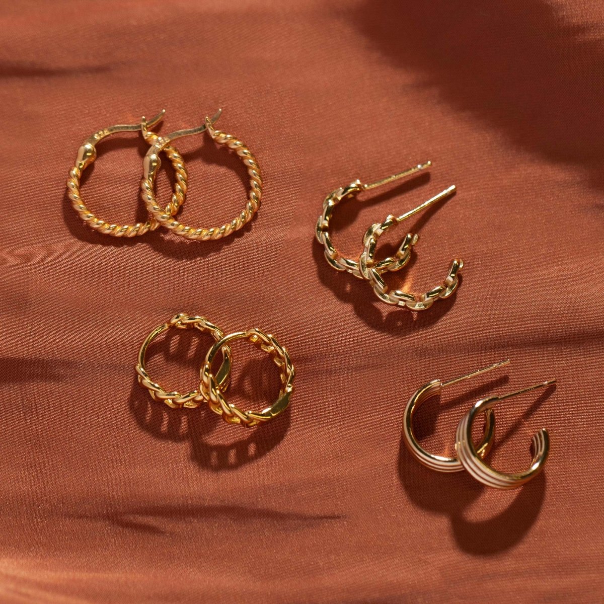 Gold vermeil twisted rope hoops and C-hoops in several sizes, arranged on terracotta fabric