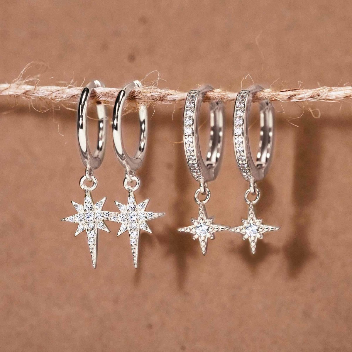 Sterling silver starburst drop huggie hoops with clear pavé stones, shown on a string