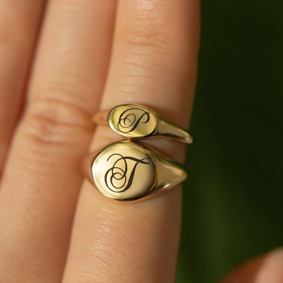 Two gold vermeil oval signet rings each engraved with an initial, shown stacked on a finger