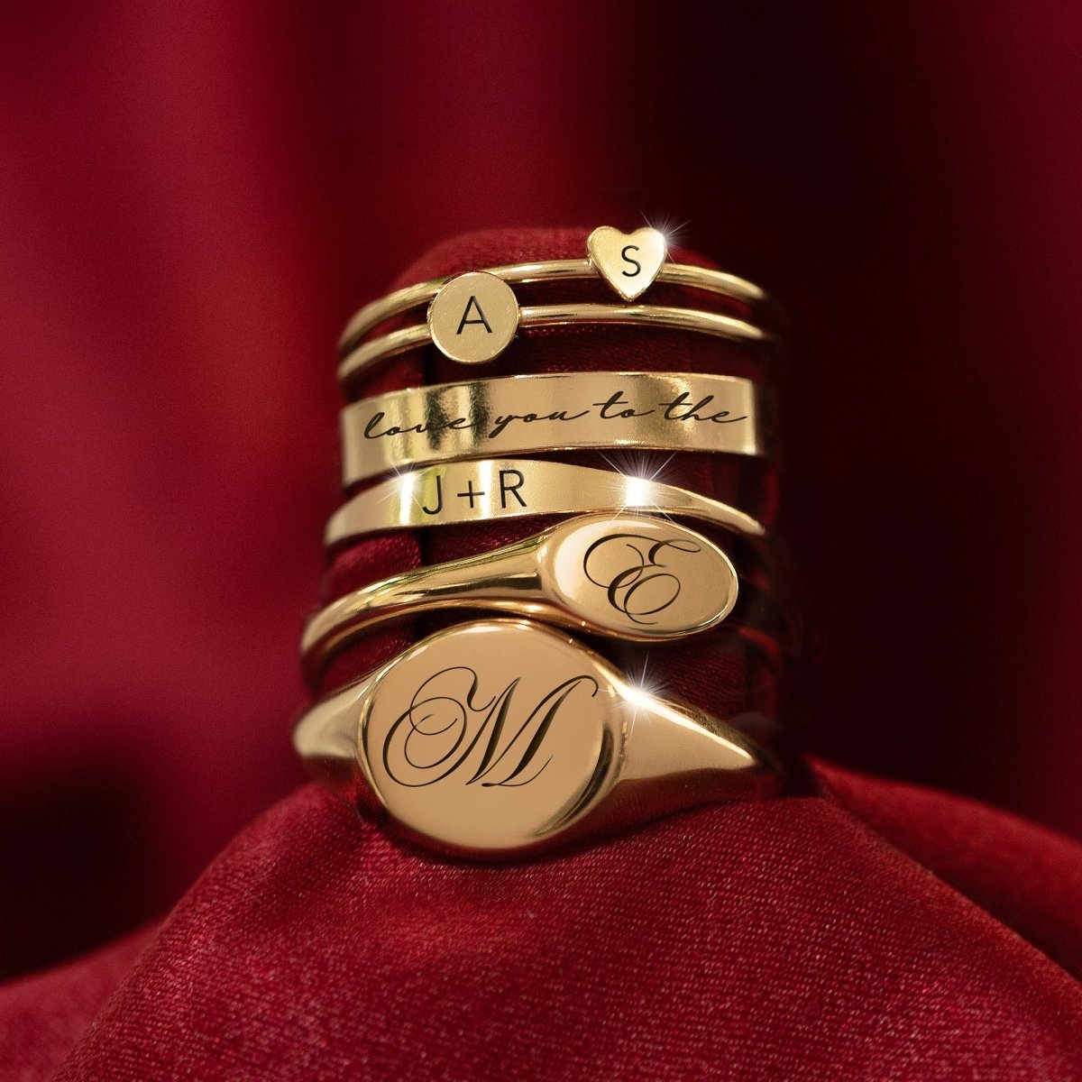 Stack of gold-filled engraved rings with disc, heart, signet and band styles, on red velvet