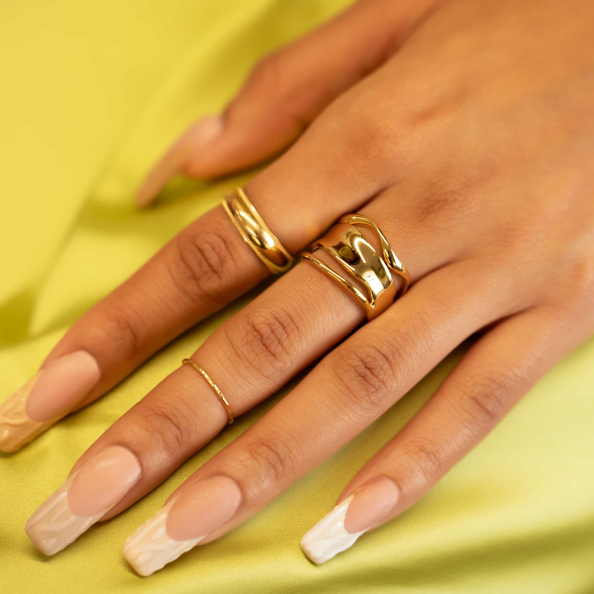 Gold-filled thin textured band ring shown on a model's finger on a yellow background