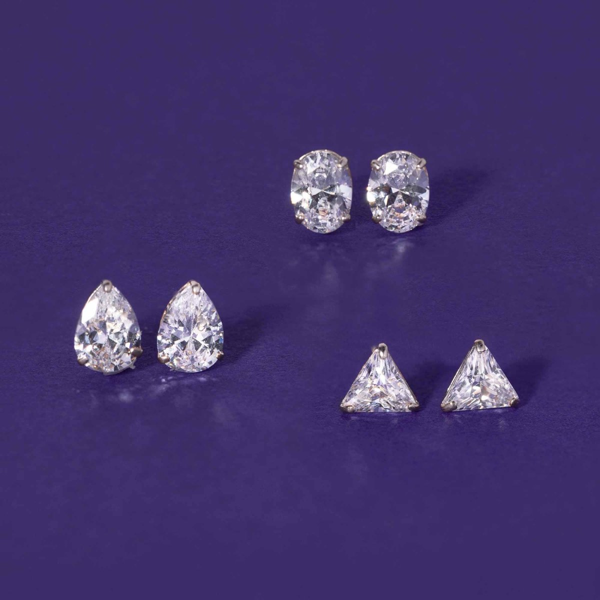 14K white gold pear, oval, and triangle stud earrings with clear stones, on a purple background