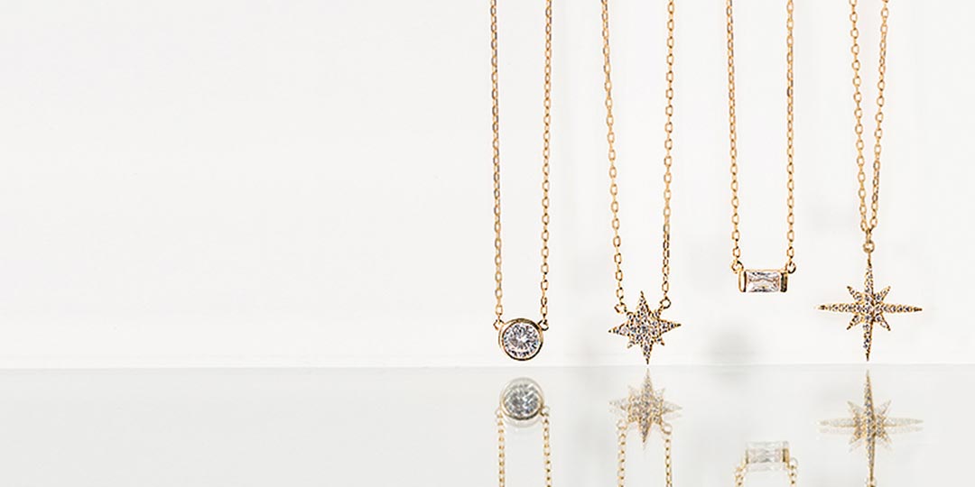 Four gold pendant necklaces with solitaire, starburst, and baguette crystal pendants