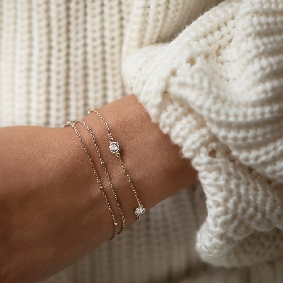 Sterling silver white zirconia station bracelet stacked on a model's wrist with a white sweater