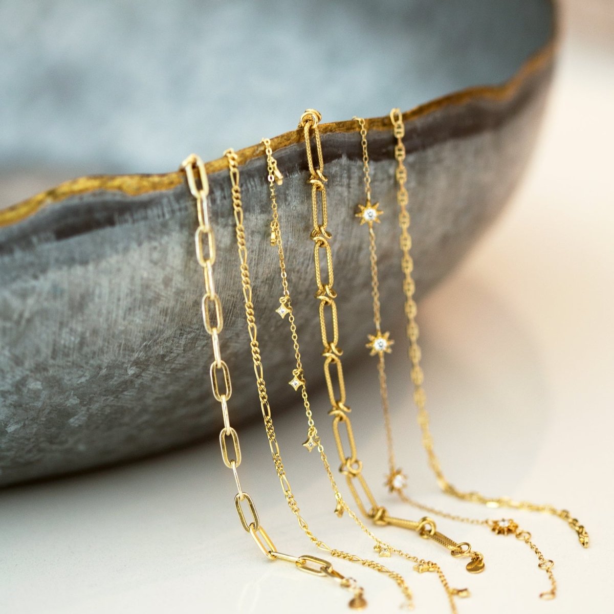 Gold vermeil star dangle bracelet shown among layered gold chain bracelets draped over a stone dish