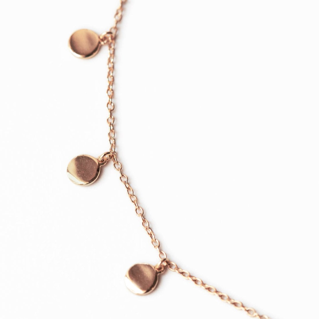 Rose gold vermeil bracelet, close-up of round disc charms on a fine chain, on a white background