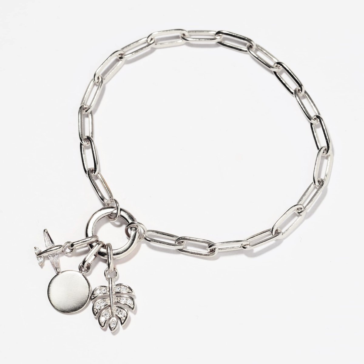 Sterling silver paperclip chain bracelet with a disc, leaf and clear stone charm cluster, on a white background