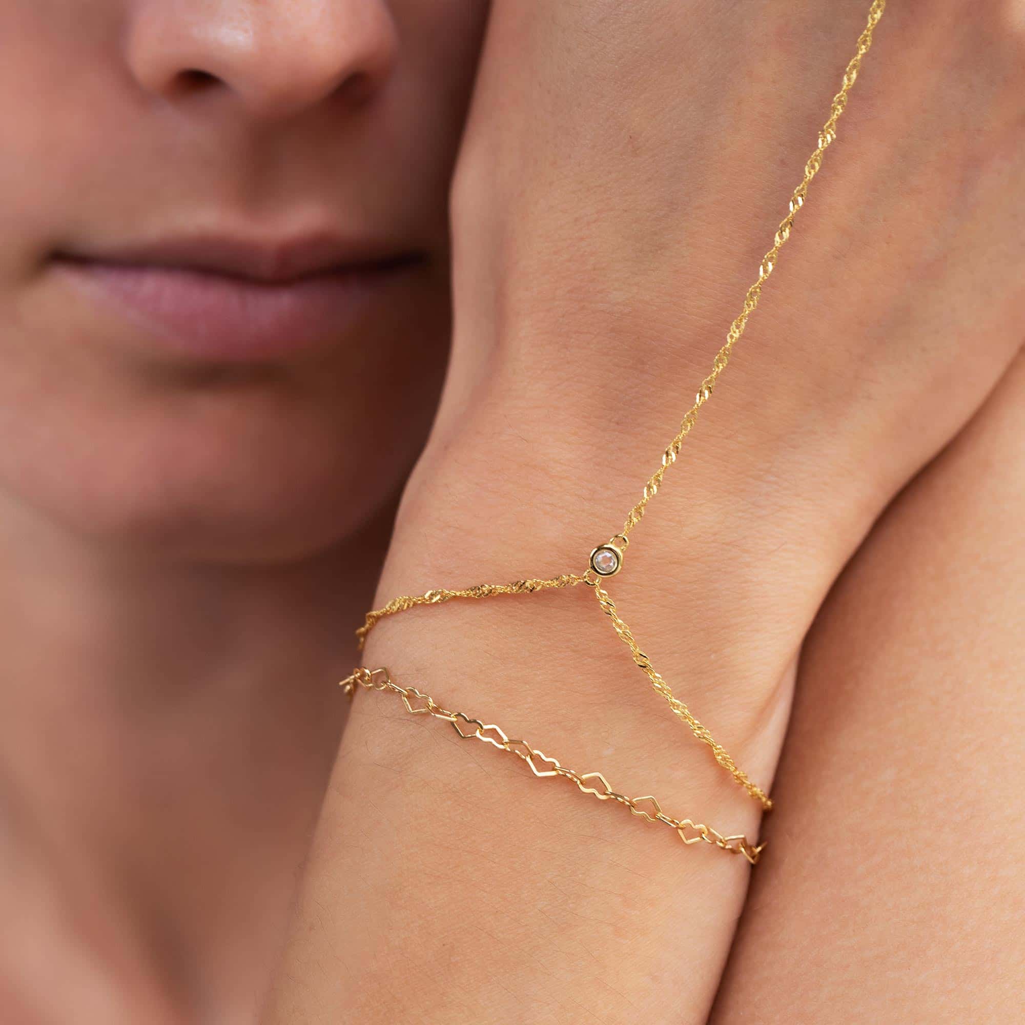 Gold vermeil handchain with a bezel-set clear stone, shown on a model's hand near her face