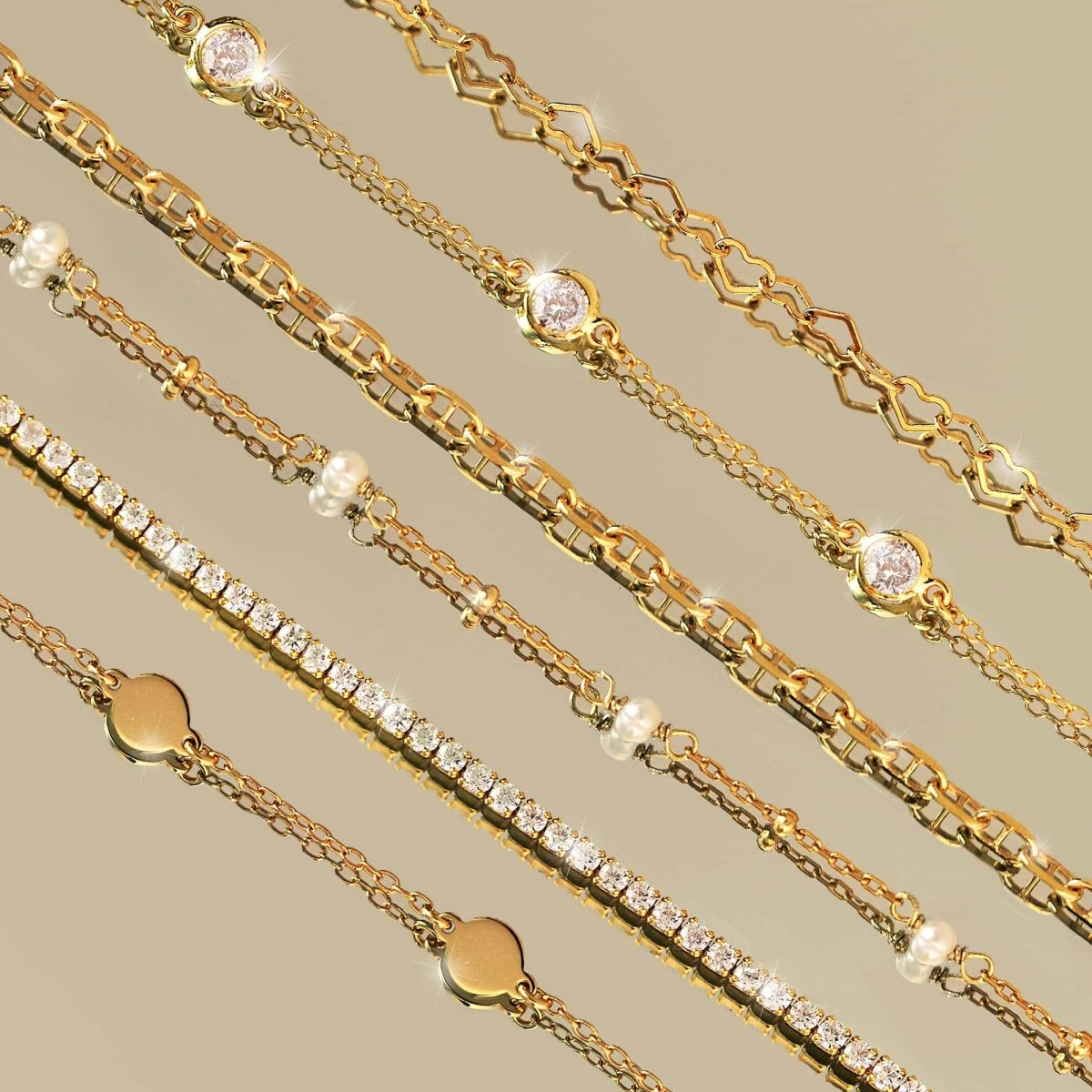 Close-up of gold vermeil dainty crystal line bracelet with white zirconia, layered among other chain bracelets