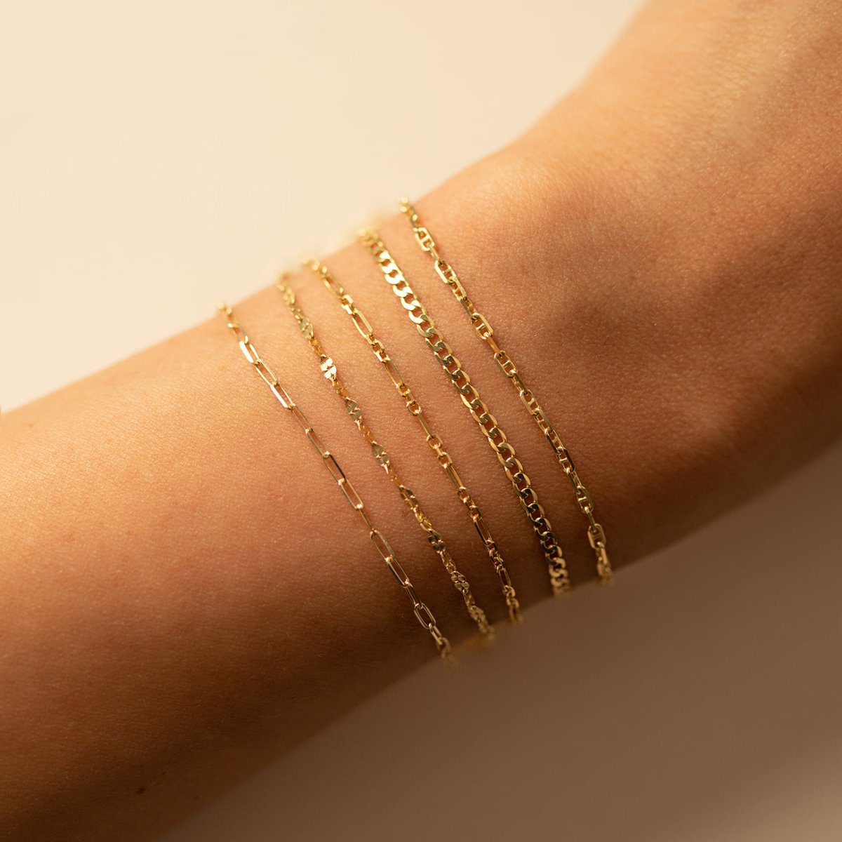 14K gold Marina chain bracelet stacked with other thin chains, shown on a model's wrist