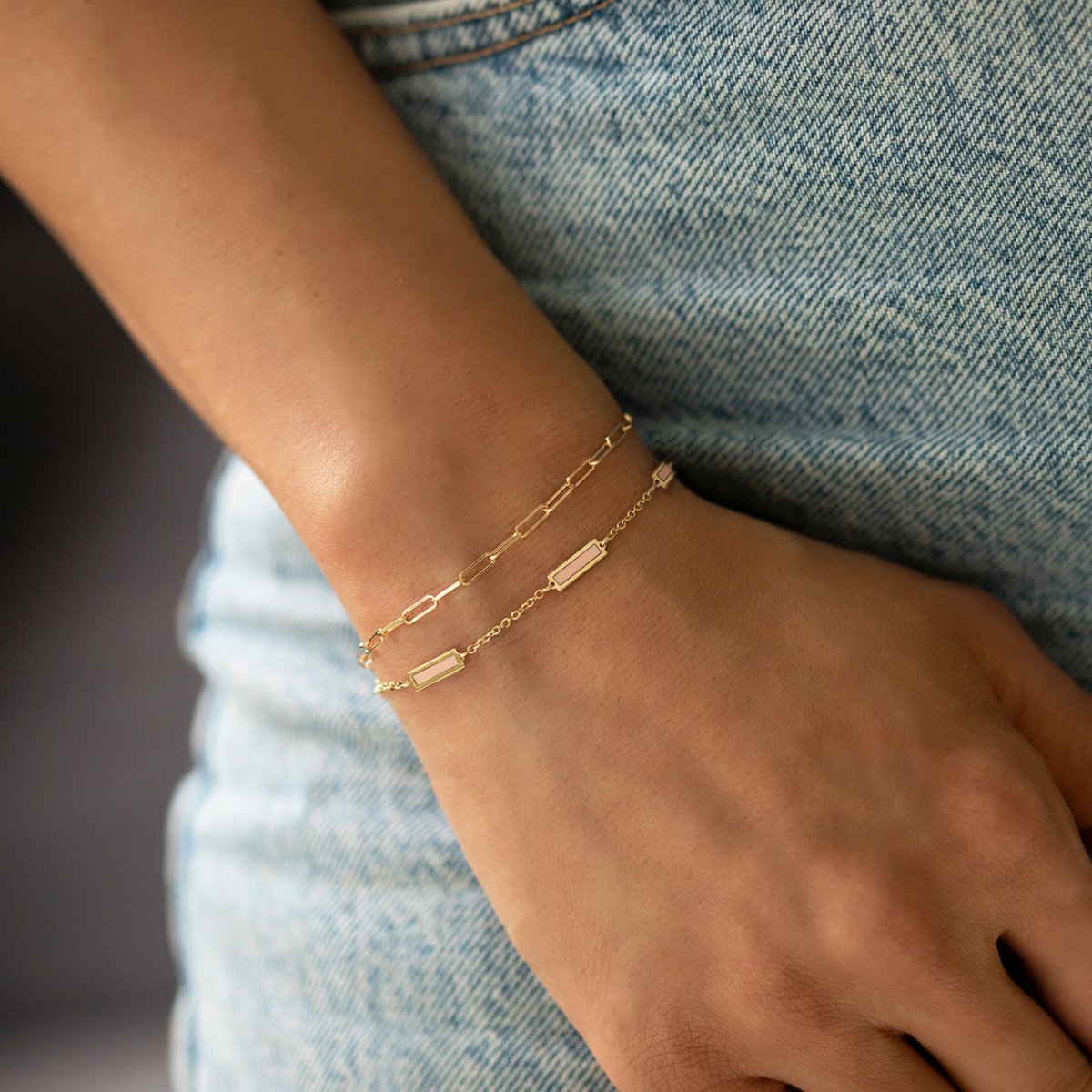 14K gold rose quartz bar bracelet layered on a chain, shown on a model's wrist