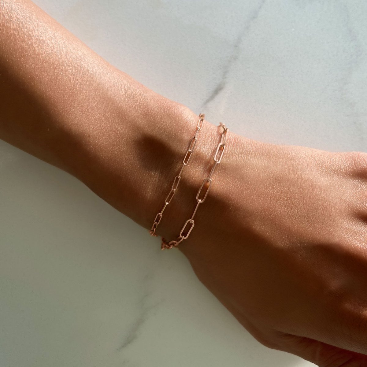 14K rose gold paperclip chain bracelets among gold chains and a gemstone-station chain on white marble
