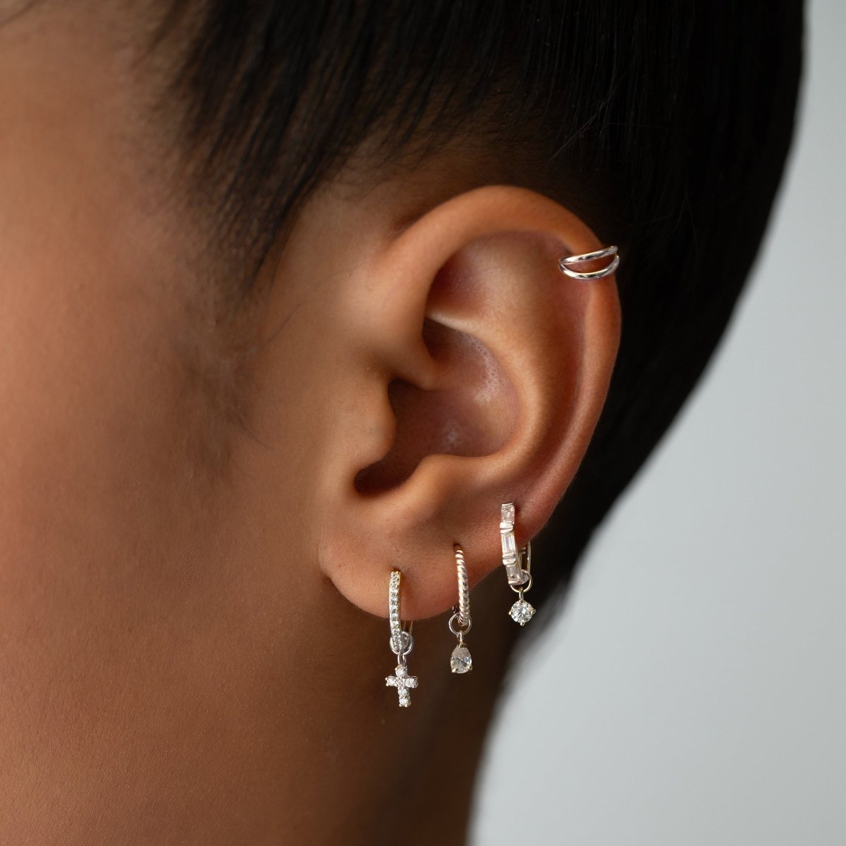 14K white gold pear moissanite charm on a hoop, shown in an ear stack on a model's lobe