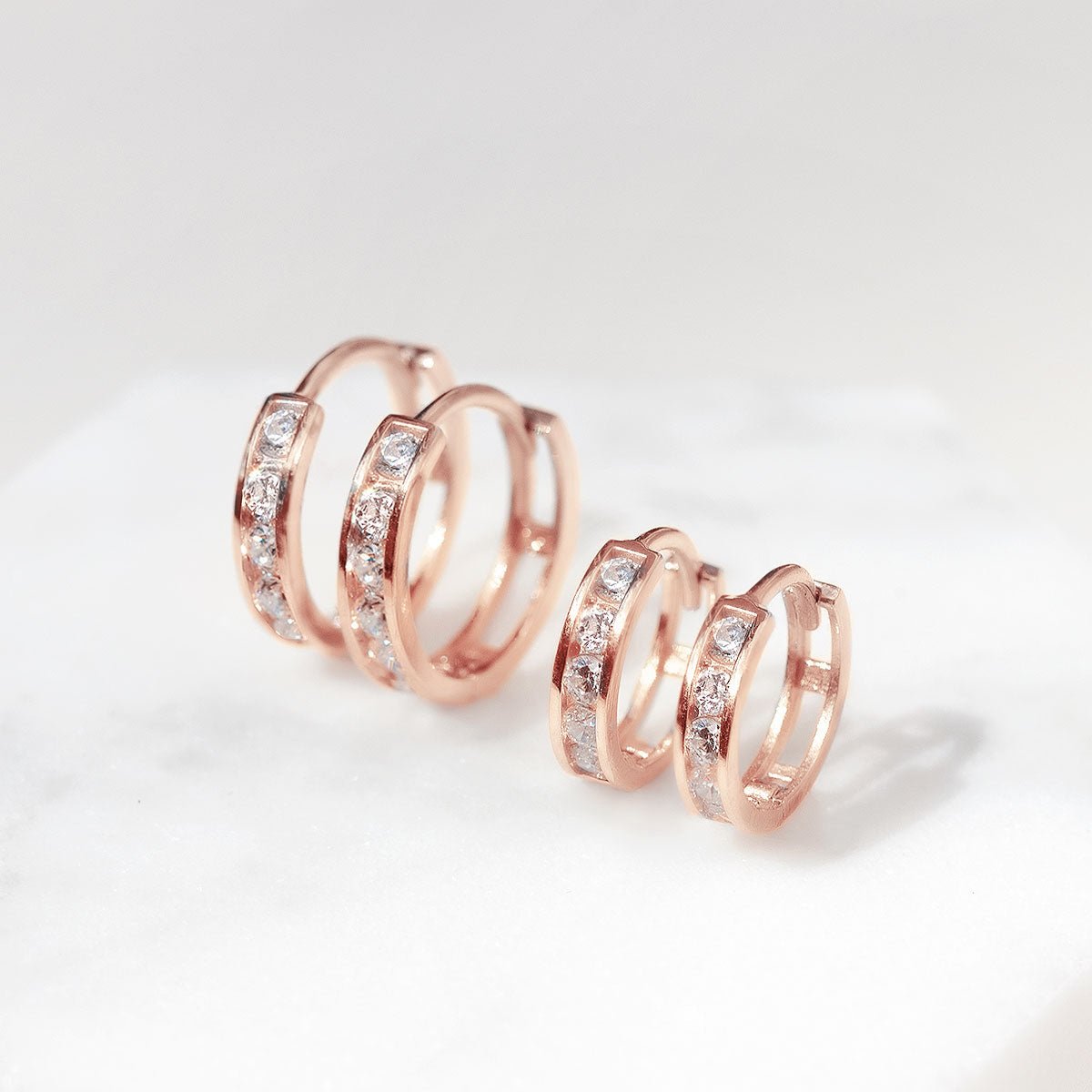 Rose gold vermeil huggie hoops in two sizes with clear cubic zirconia, on white marble