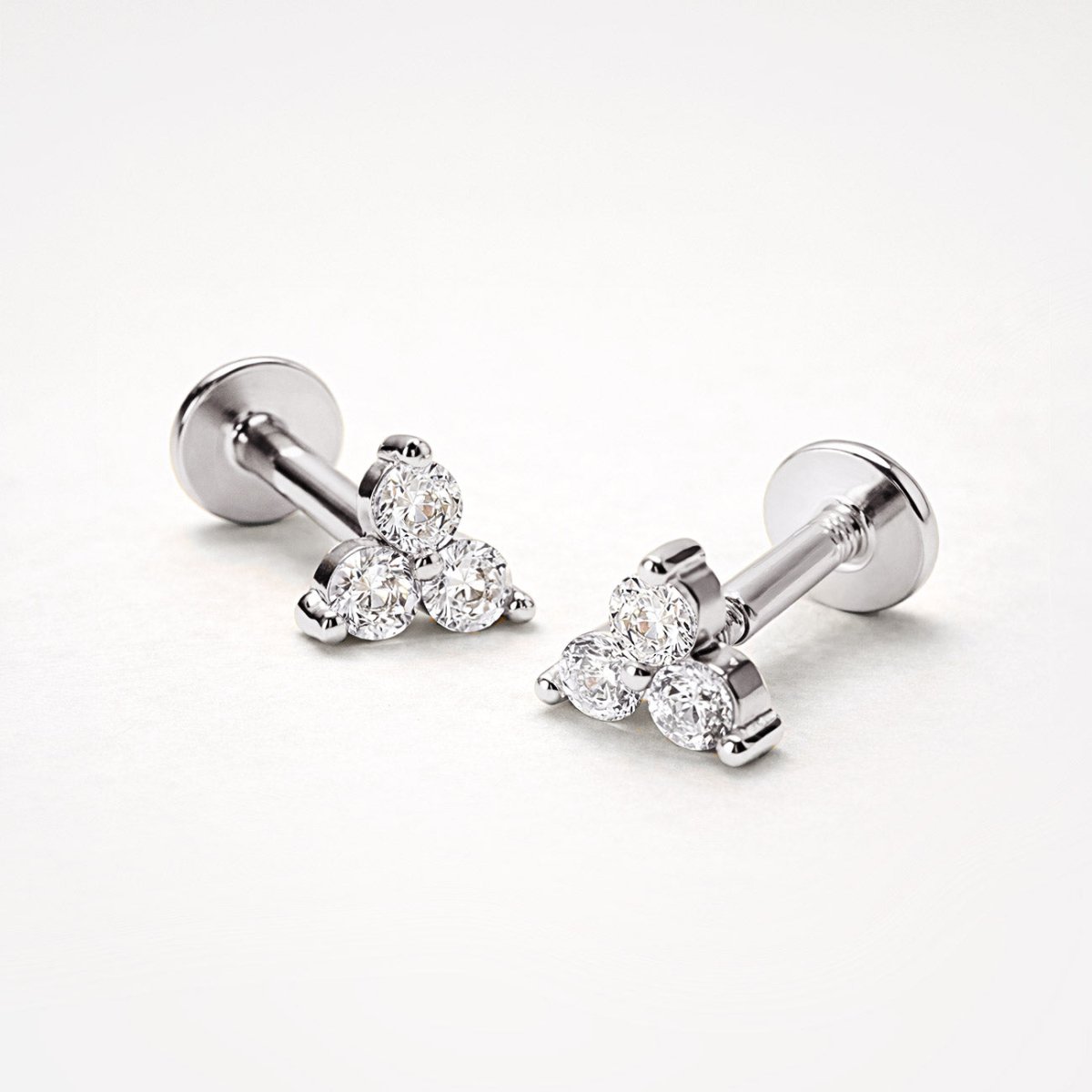 Pair of sterling silver trio white zirconia flat back studs, close-up detail on a cream background