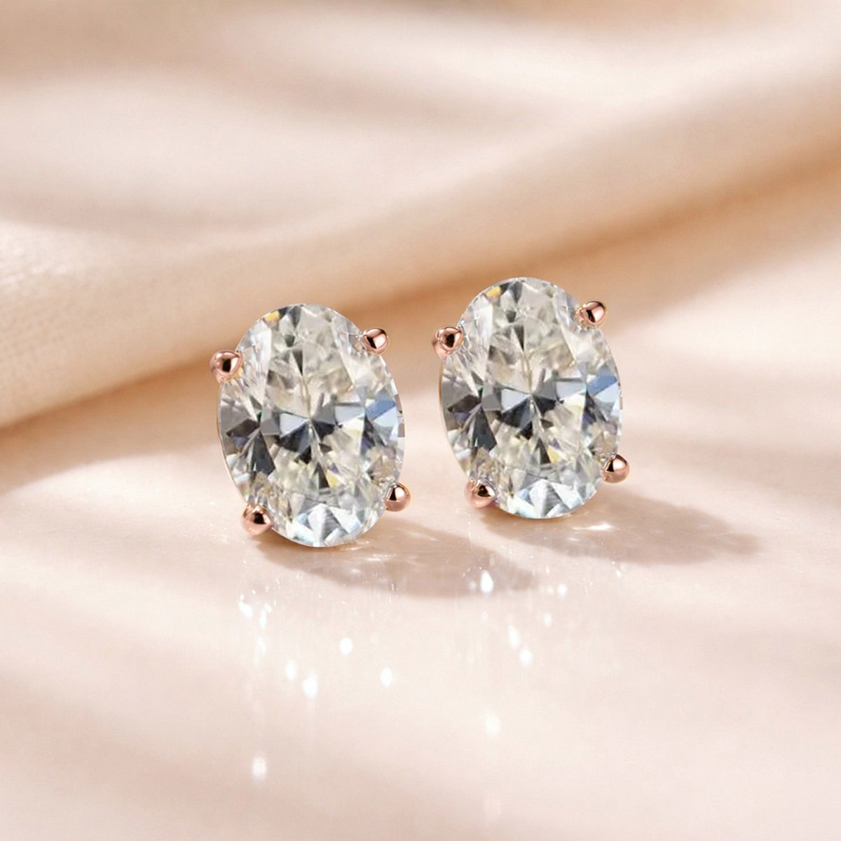 Rose gold vermeil oval studs with clear white zirconia stones, shown on cream fabric