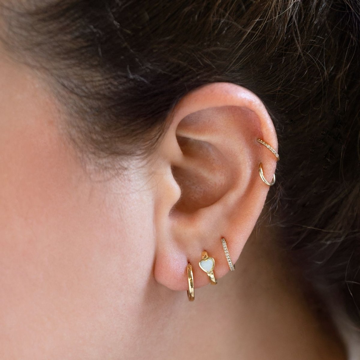 Gold hoop, opal heart huggie, and pavé hoops stacked on a model's ear