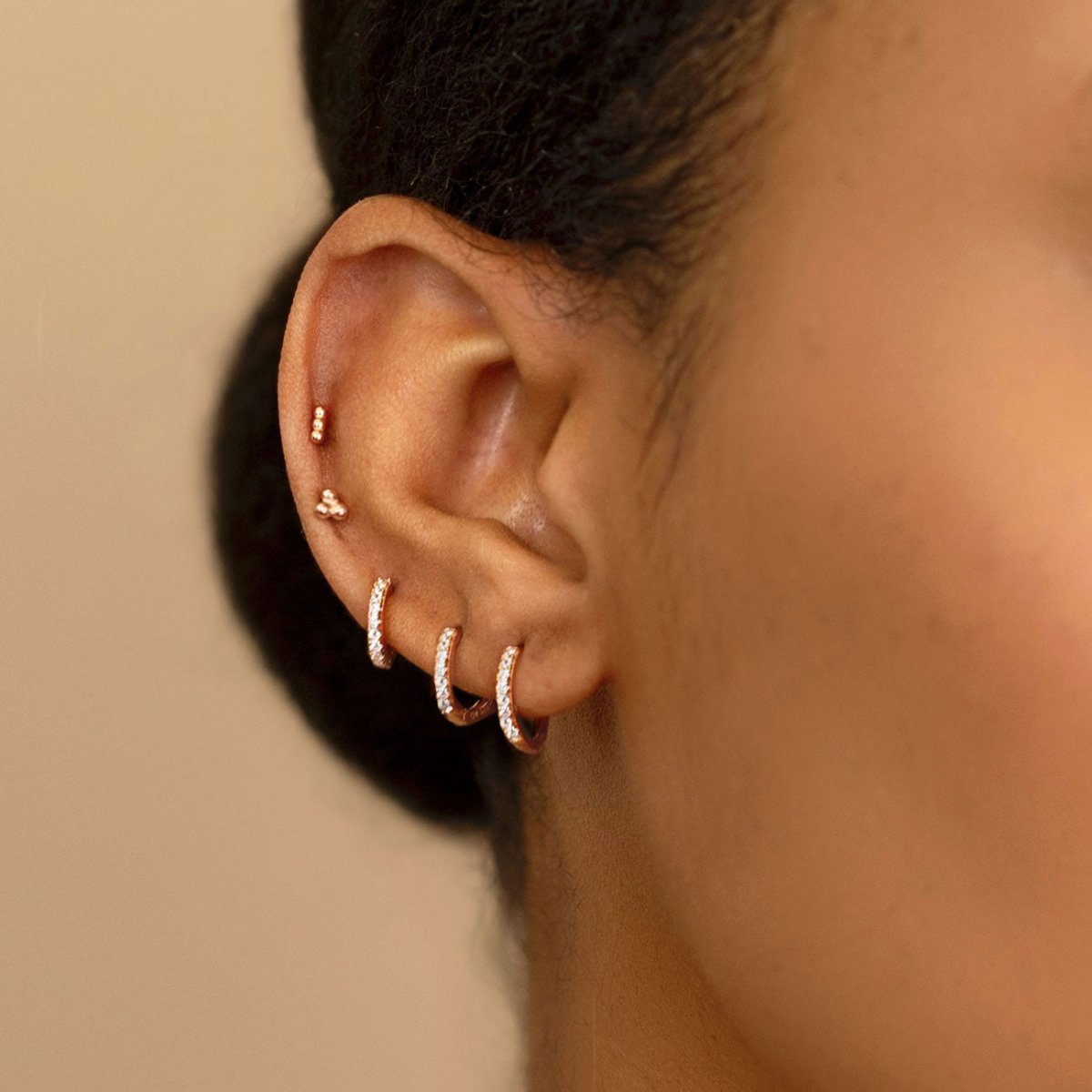 Rose gold vermeil three-ball cluster stud worn in an upper-lobe piercing, shown on a model's ear