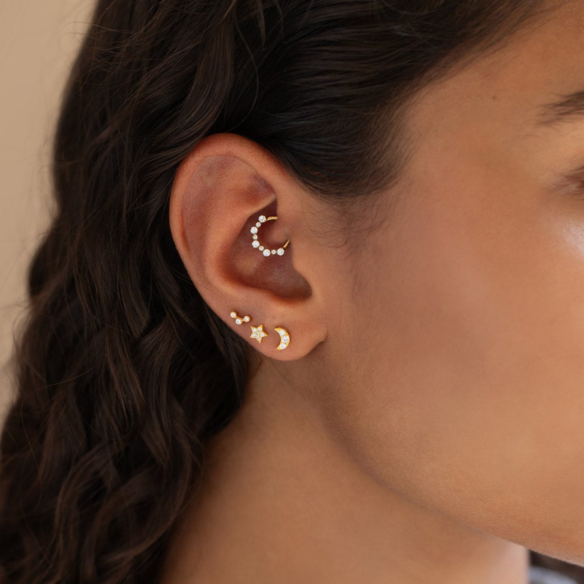 Gold clicker hoop and moon and star studs with clear stones, shown in a model's daith and lobe piercings