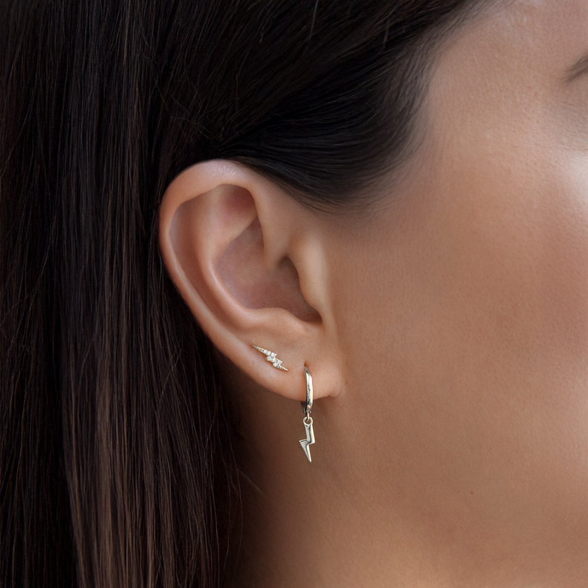 Sterling silver lightning bolt charm huggie hoop, shown on a model's ear