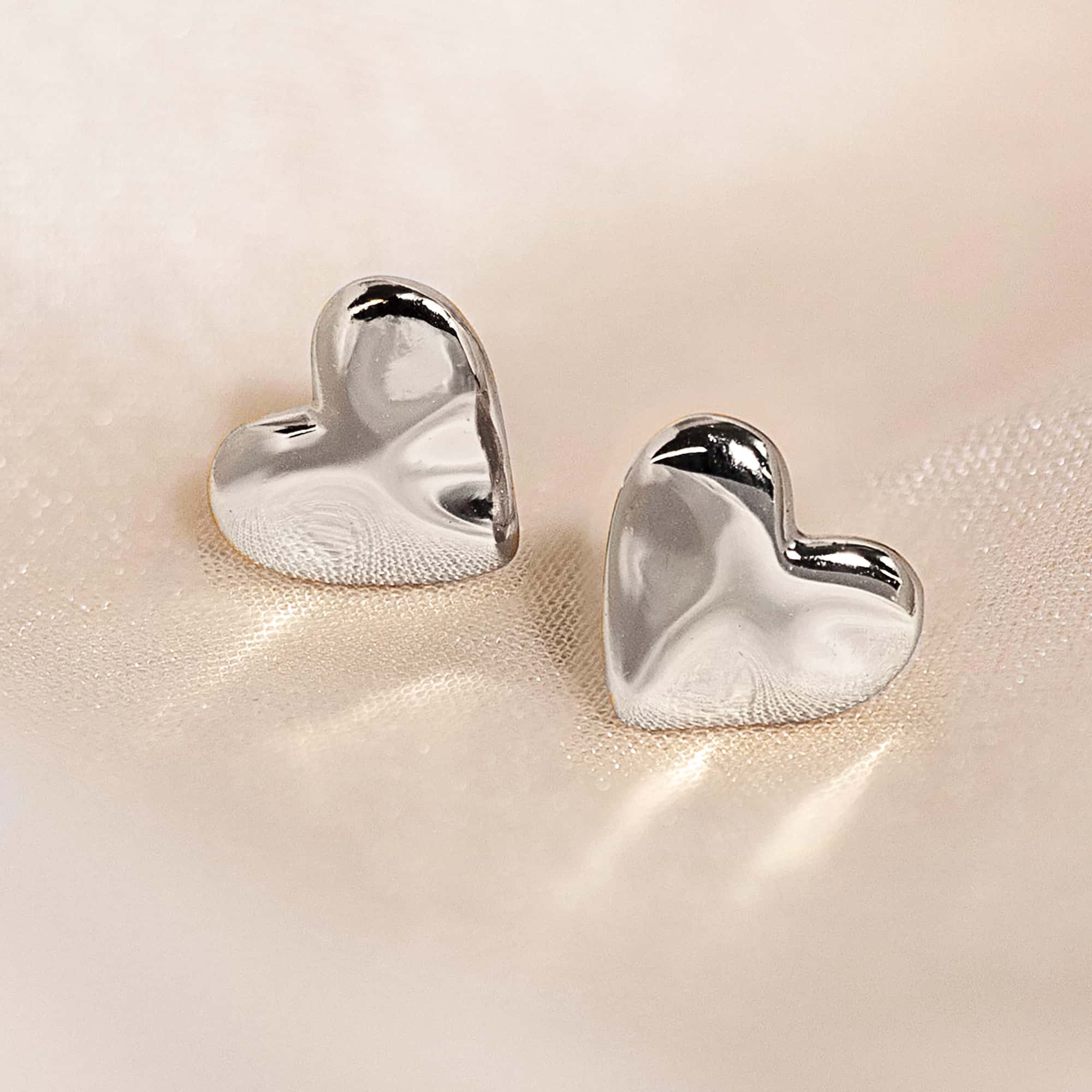 Sterling silver puffed heart stud earrings with a smooth high-shine finish, on a cream background